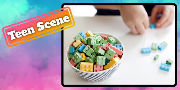 Candy LEGO game pieces in a bowl with a child's hands putting them together.